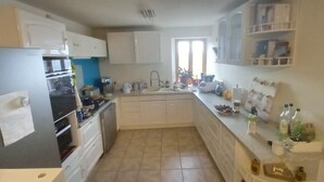 A kitchen with white cabinets, a refrigerator, an oven, a sink, and a countertop with various items. - Character house (PUIMISSON)