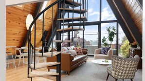 A spacious loft with a wooden interior, a spiral staircase, and large windows offering a view of the outdoors.