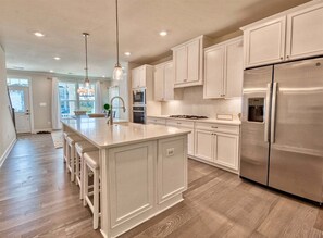 A kitchen with white cabinets, a stainless steel refrigerator, and a central island with stools.