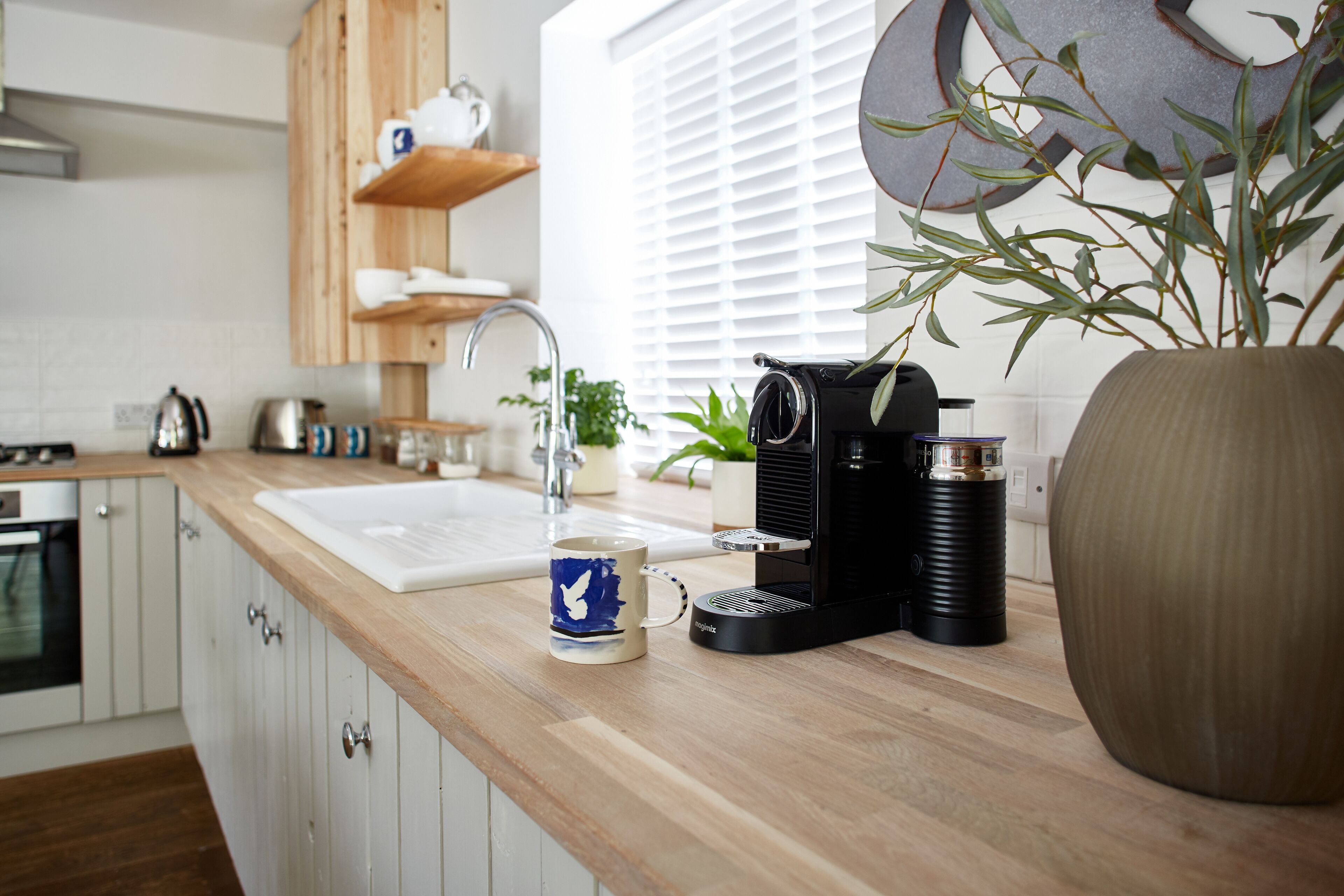 Een moderne keuken met houten kastjes, een koffiezetapparaat, een waterkoker en een potplant.