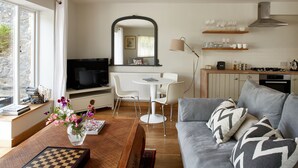 Un salon moderne avec un canapé, une table basse et un jeu d’échecs. On y trouve également un coin repas avec une table et des chaises, ainsi qu’une cuisine équipée d’une cuisinière et d’étagères.