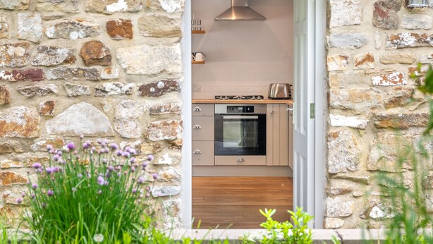 Une cuisine aux murs de pierre, dotée d’une cuisinière et d’un four modernes, ainsi que d’armoires en bois.