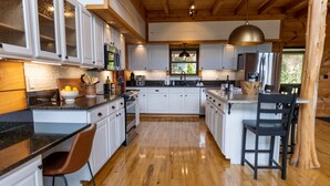 A modern kitchen with white cabinets, a central island, and a wooden floor. - Luxury 5 BR Cabin with Hot Tub and Views!  (Townsend)