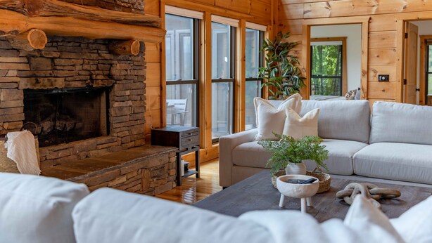 A cozy living room with a stone fireplace, a sofa, and a coffee table. - Luxury 5 BR Cabin with Hot Tub and Views!  (Townsend)