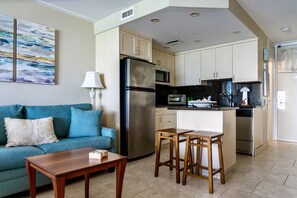 Espaço compacto com cozinha compacta, sofá, mesa de centro e um banquinho.