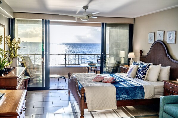 A bedroom with a large bed, a balcony with a view of the sea, and a ceiling fan. - WOW! What a view!!! Oceanfront Condo in Ka’anapali! King Bed! (Lahaina)