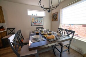 A dining area with a table set for four, chairs, a chandelier, a window with blinds, and a poster on the wall.