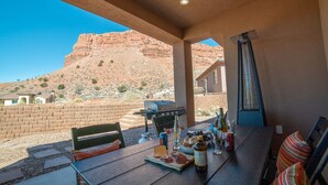 Un patio al aire libre con una mesa lista para comer, una parrilla y vistas a formaciones rocosas rojas.