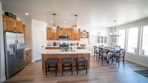 Una cocina moderna con armarios de madera, un refrigerador de acero inoxidable, una isla central con taburetes y un comedor con candelabro.
