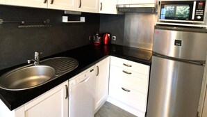 Une cuisine moderne avec des armoires blanches, un évier en acier inoxydable, un lave-vaisselle, un four à micro-ondes et un réfrigérateur.