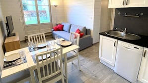 Une cuisine compacte avec un coin repas, des meubles blancs, un plan de travail noir et une vue sur l’extérieur.