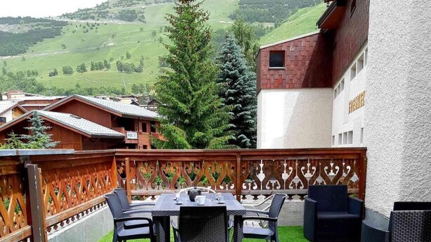 Une terrasse extérieure avec une table et des chaises, entourée d’une clôture en bois et offrant une vue sur un paysage montagneux.