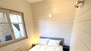 Un petit lit, bien fait, dans une pièce aux murs blancs et dotée d’une fenêtre.