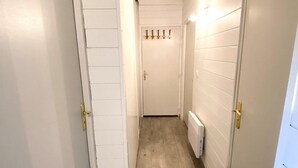 Un couloir étroit aux murs blancs et au plancher en bois, qui mène à une porte près de laquelle se trouve un porte-manteau.