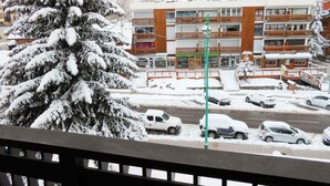 Un edificio a più piani con un ristorante al piano terra, circondato da alberi imbiancati dalla neve e auto parcheggiate.