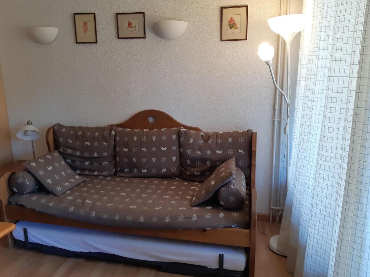 A sofa bed with a patterned cover, a side table, a floor lamp, and framed pictures on the wall.