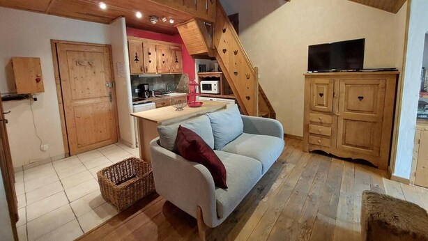 A cozy living room with a sofa, a TV, wooden cabinets, and a kitchen area with a microwave. - 100m from ski slopes, 4th floor, tv, ski locker, 44m², Les 2 Alpes (Les Deux Alpes)