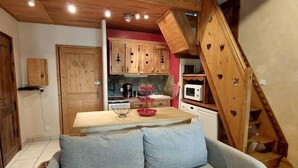 A cozy living area with a wooden staircase, a kitchen with red appliances, and a grey sofa. - 100m from ski slopes, 4th floor, tv, ski locker, 44m², Les 2 Alpes (Les Deux Alpes)