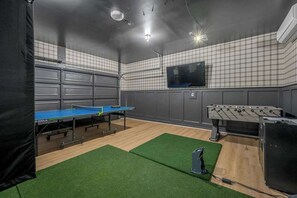 Une pièce équipée d’une table de ping-pong, d’un baby-foot et d’un téléviseur fixé au mur.