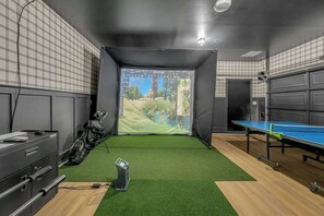 Ein Raum mit einem grünen Kunstrasen, einem Tischtennis-Tisch, einer Golfbag und einem Computerarbeitsplatz.