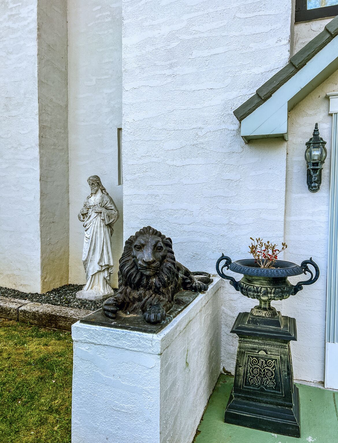A statue of a lion and a figure on a pedestal, a decorative urn with plants, and a wall-mounted light fixture.