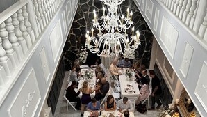 A formal dining hall with white tables and chairs, a chandelier, and a stone wall. - Smithmore Castle (Spruce Pine)