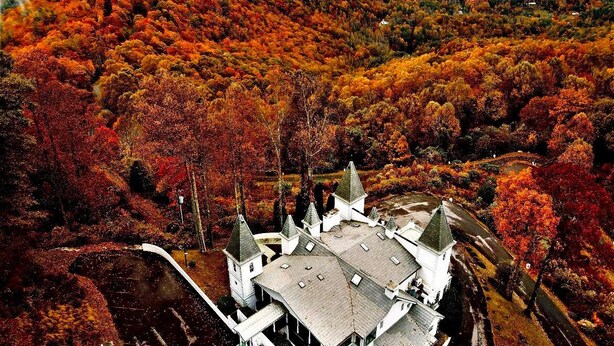 A large, white building with multiple towers, surrounded by a forested area with autumn foliage. - Smithmore Castle (Spruce Pine)