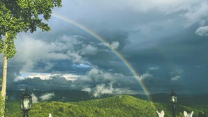 A white balustrade with a view of a lush green hill and a rainbow. - Smithmore Castle (Spruce Pine)