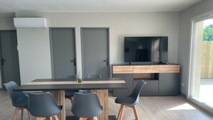 Une cuisine moderne avec un coin repas, comprenant une table en bois, des chaises grises, un téléviseur encastré et une grande fenêtre.