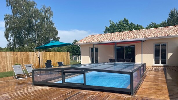 Une piscine dotée d’une structure en verre, d’une terrasse en bois, de mobilier d’extérieur et d’un patio couvert.