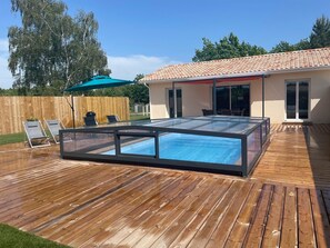 A swimming pool with a glass enclosure, wooden deck, outdoor furniture, and a covered patio area. - 4-bed house with heated and covered swimming pool ( Maison Océan) (Grayan-et-l'Hôpital)