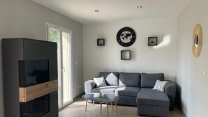 Un salon moderne avec un canapé d’angle gris, une table basse en verre et un meuble de rangement pour appareils multimédias de couleur sombre.