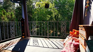 Ein Balkon mit einem gemusterten Teppich, Korbmöbeln und einer hängenden Pflanze.