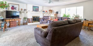 A living room with a brown leather sofa, a television, a fireplace, and various decorative items on shelves. - Steps to Sugar Loaf Trail • 2 Baths • King bed • 1200 SqFt (Sedona)