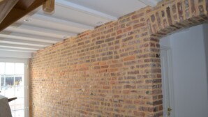 Une pièce aux murs en briques apparentes, avec une porte blanche et une fenêtre donnant sur l’extérieur.