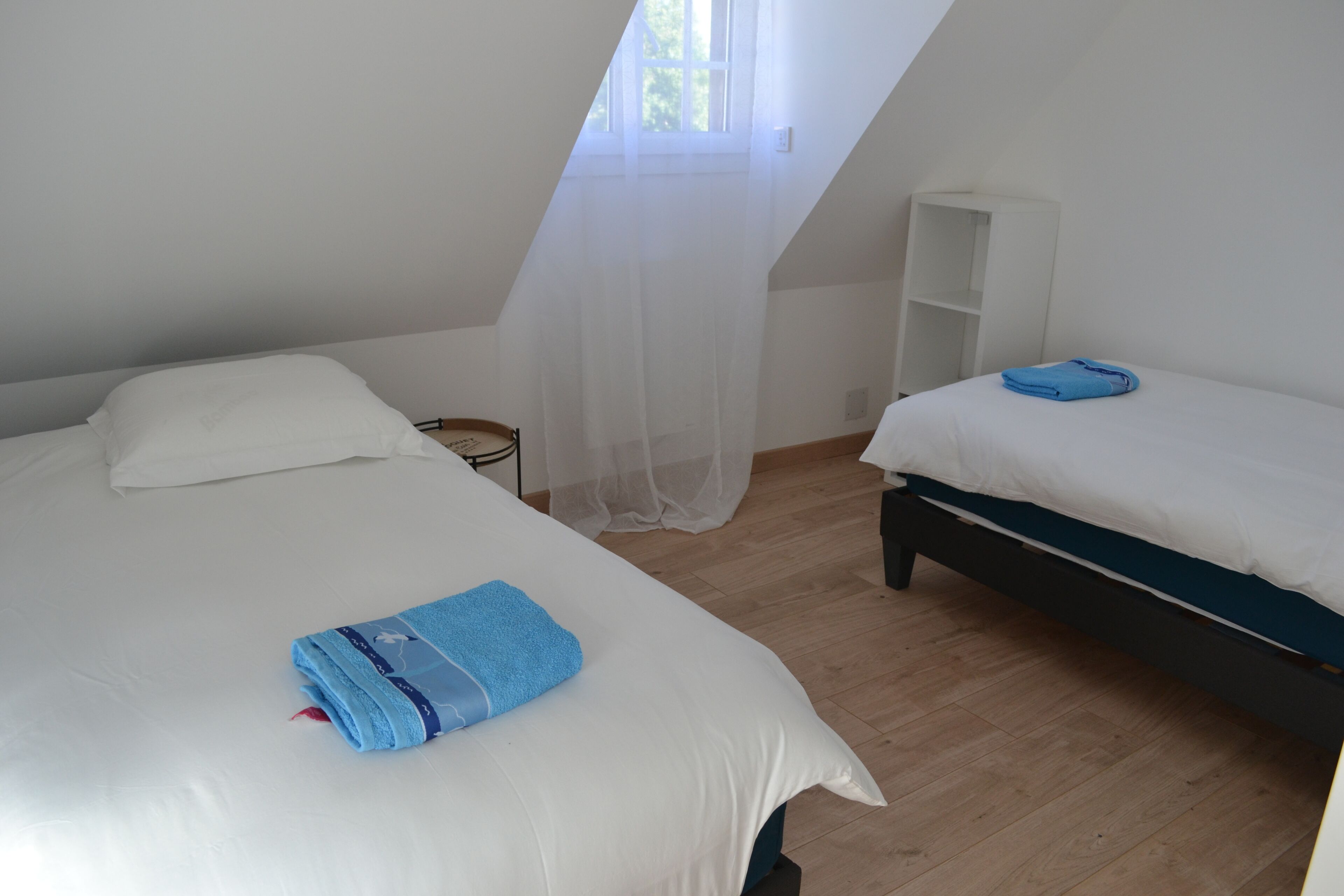 A room with two beds, a white wardrobe, and a window with sheer curtains.