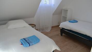 A room with two beds, a white wardrobe, and a window with sheer curtains.