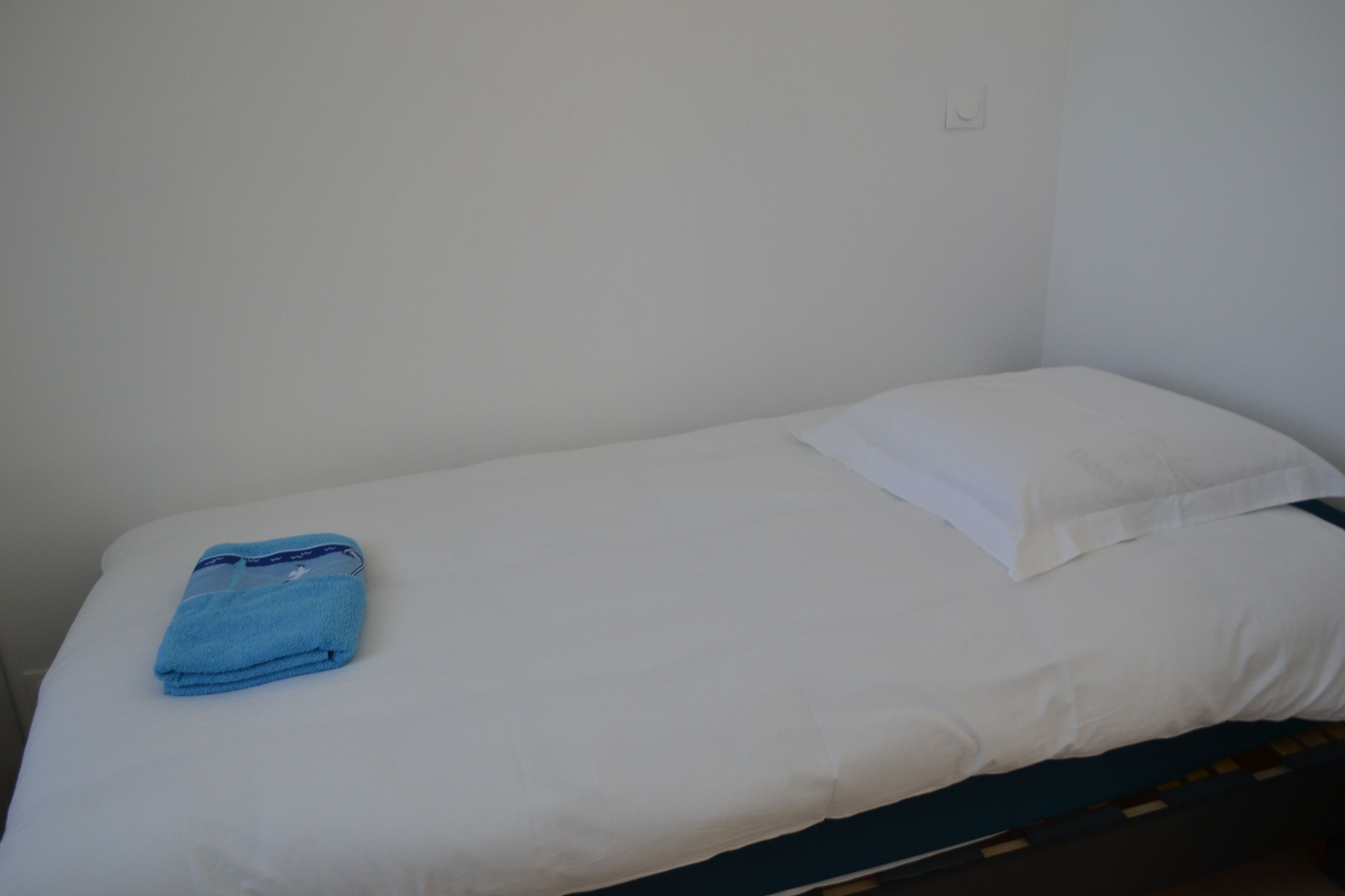 Een kleine kamer met een eenpersoonsbed, witte beddengoed en een blauwe handdoek op het bed.