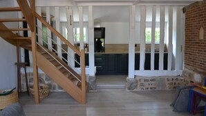 Un vaste espace de vie agrémenté d’un escalier en bois, une cuisine avec des rampes blanches et un mur en pierre.