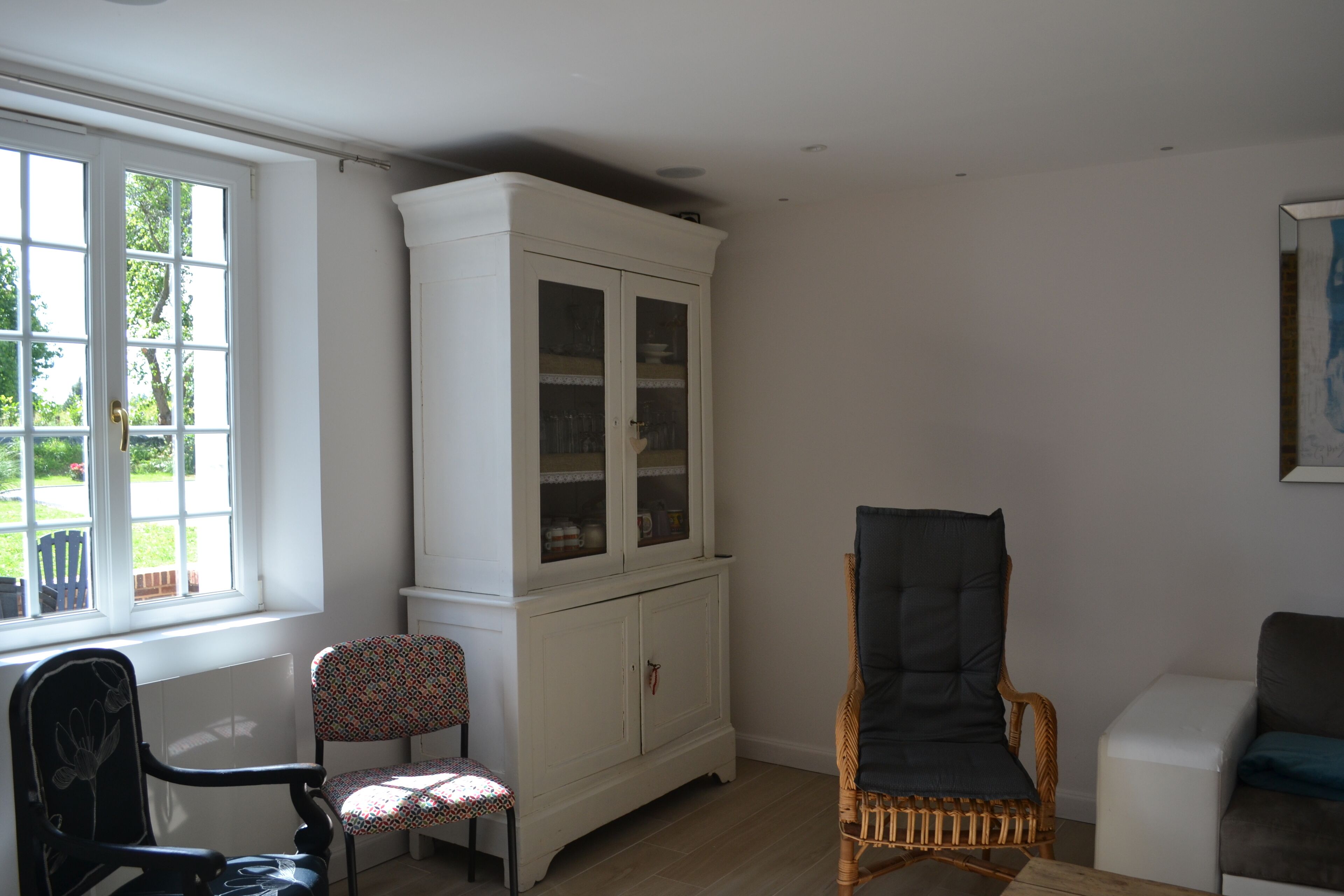 A room with a white cabinet, a wicker chair, a patterned chair, and a white sofa.