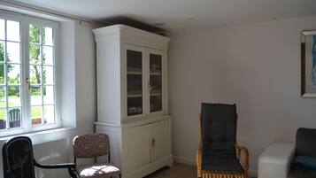 A room with a white cabinet, a wicker chair, a patterned chair, and a white sofa.
