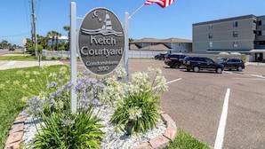 Een bordje voor Ketch Courtyard Condominiums, met een vlag en een parkeerplaats op de achtergrond.