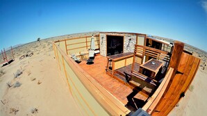 A desert-themed outdoor area with a wooden deck, seating, and a stone wall. - Unique off Grid Desert Retreat, California, USA (Hesperia)