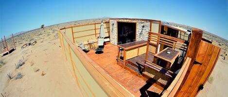 A desert-themed outdoor area with a wooden deck, seating, and a stone wall.