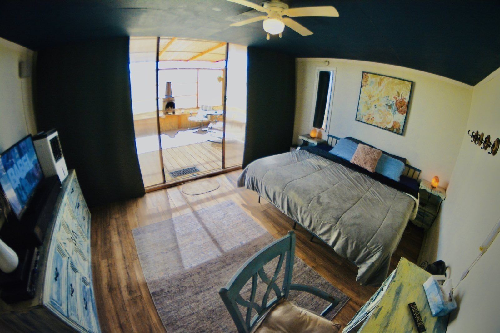 A bedroom with a bed, a desk, a chair, a TV, and a ceiling fan.