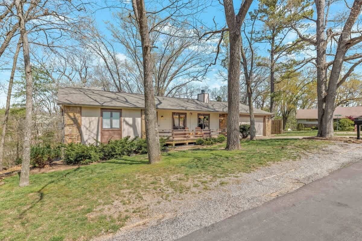 A single-story house with a front porch, surrounded by trees and a gravel driveway.