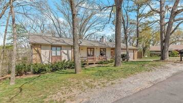 A single-story house with a front porch, surrounded by trees and a gravel driveway.