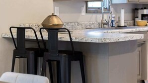Et køkken med en granitbordplade, to sorte barstole og en hængende lampe.