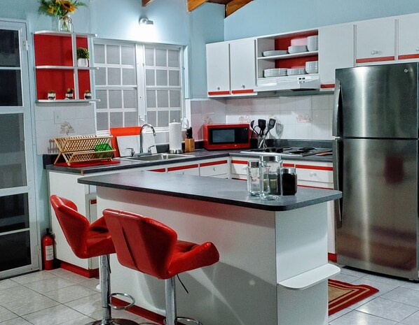 Una cocina moderna con una isla central, taburetes rojos, un refrigerador de acero inoxidable y armarios blancos.