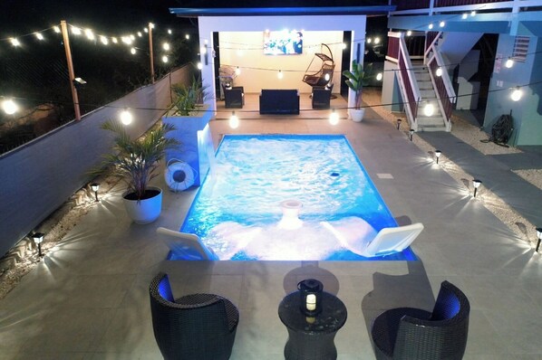 A swimming pool with a hot tub, surrounded by outdoor seating and string lights.